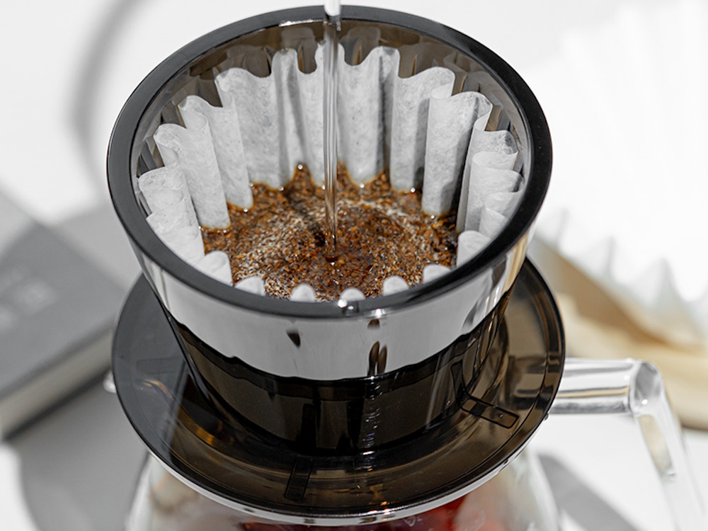 A close up of water being poured over coffee grounds in a pour over brewer.