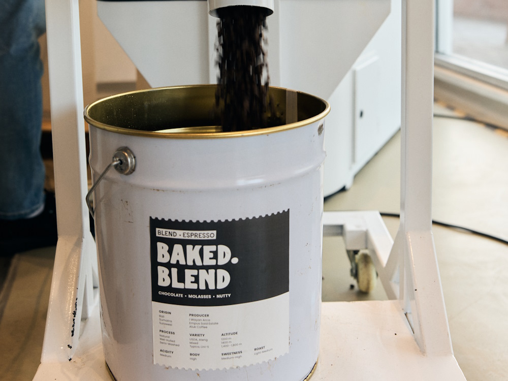A roaster empties coffee beans into a metal tin in a roastery.