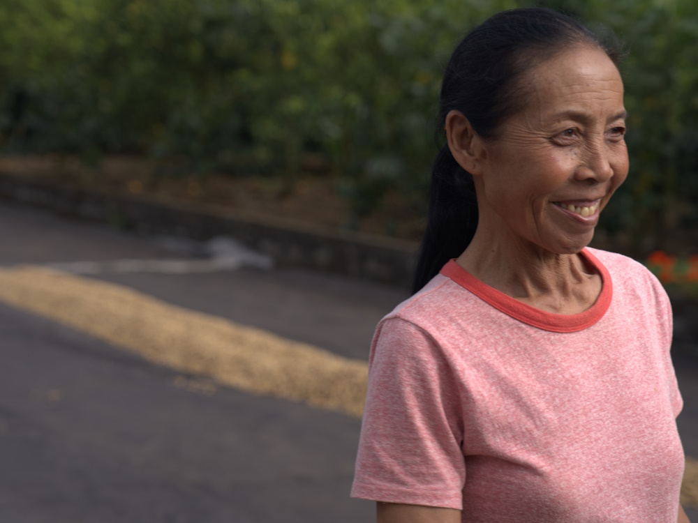 A female Indonesian farmer stands next to coffee drying beds.