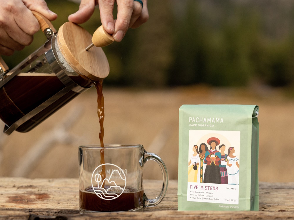 A person pours brewed coffee from a French press into a glass.