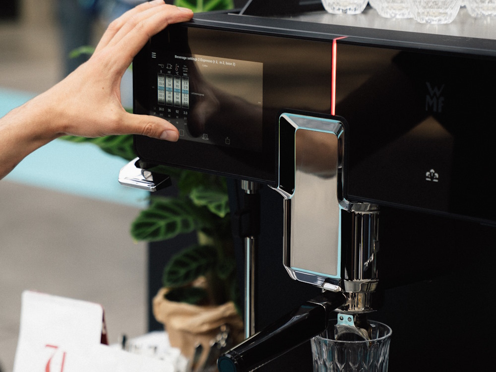 A person uses a WMF automatic machine at World of Coffee Copenhagen event.