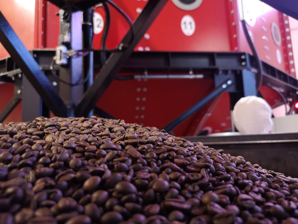 A pile of roasted coffee beans in front of an IMF machine.