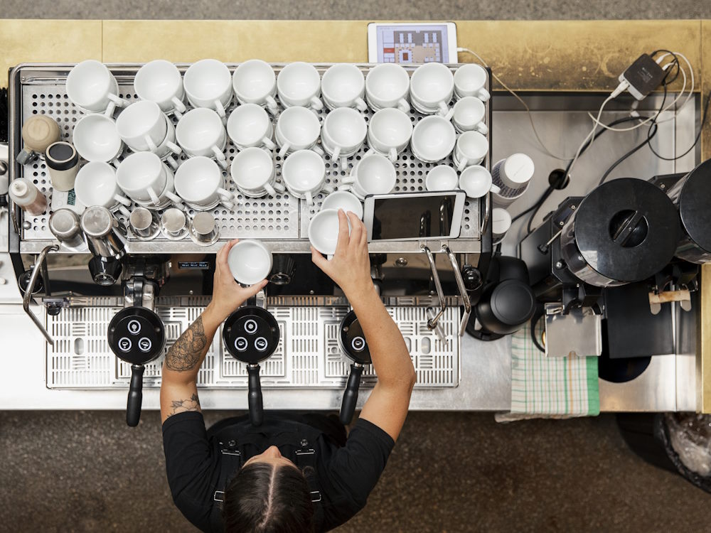 A woman stacks coffee cups on top of an espresso machine.
