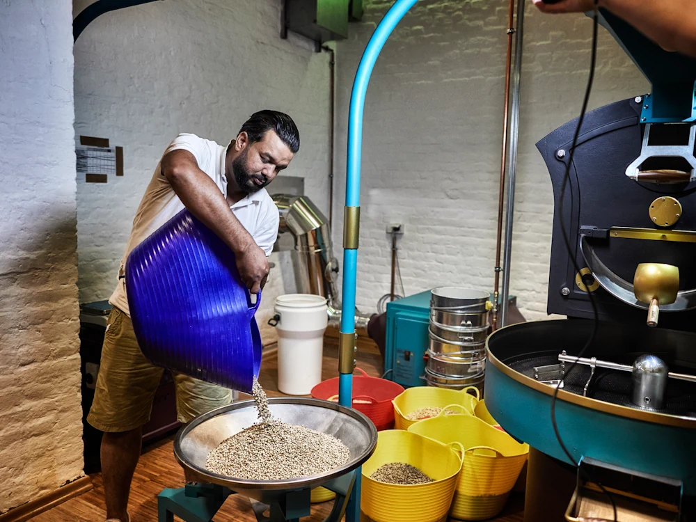 A man adds green coffee into a loading machine for a roaster.