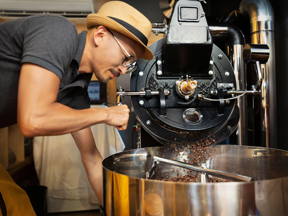 A man unloads coffee from a roaster into a cooling tray.